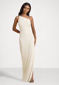 Kremowa sukienka na jedno ramię, wykonana z gładkiej tkaniny, z bocznym rozcięciem i subtelnym marszczeniem, ozdobiona metalicznym detalem na ramieniu.