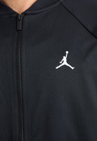 Black zip-up jacket in a smooth material, featuring a white embroidered Jumpman logo on the left chest area.