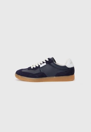 Mørkeblå joggesko laget av lær og suede, med en hvit tunge og hæl aksent, samt en teksturert gummi såle.