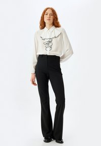 Blusa bianca con dettagli a ruffles neri, maniche lunghe, abbinata a pantaloni neri a vita alta. Aspetto alla moda e ben rifinito.