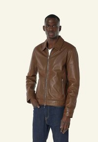 Bruine leren jas met een puntkraag, voorrits en twee zijzakken. Gekocht over een wit shirt met donkere spijkerbroeken. Soepele textuur.