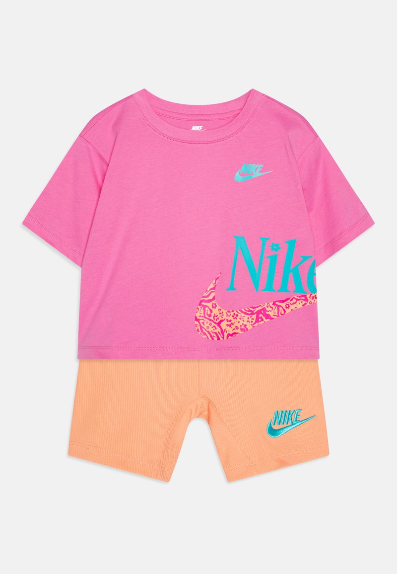 Rožinė trumpa rankovė T-maišo su mėlynomis Nike logo ir leopardų rašto akcentu, derinama su raibais oranžiniais šortais su mėlyna Nike logotipu.