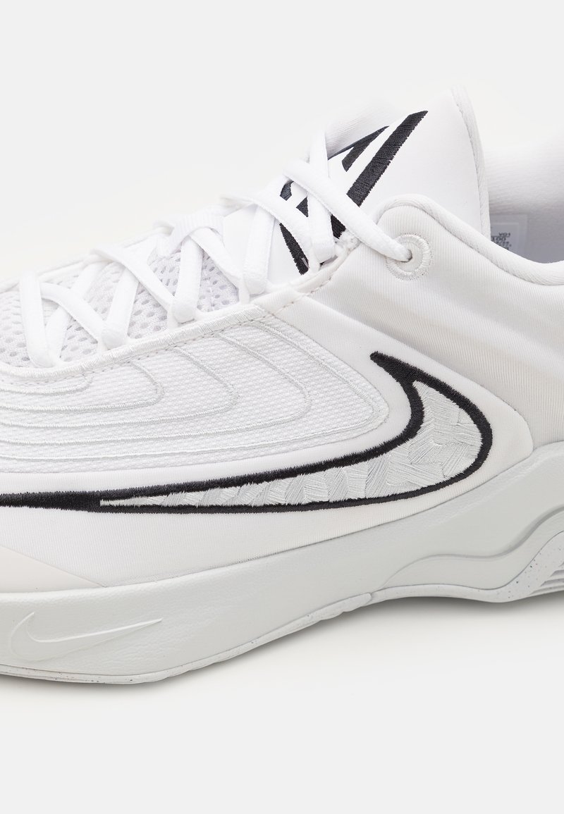 Zapatilla deportiva blanca con parte superior de malla y acentos negros. Presenta costuras texturizadas y una suela blanca duradera con un acabado suave.