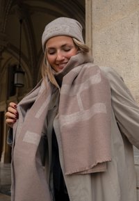 Beige wollen sjaal met een zachte textuur, voorzien van lichte geometrische patronen. Vergezeld door een bijpassende gebreide muts.