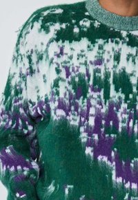 Pull en maille à motif vert et violet avec une texture duveteuse. Il présente un col rond et des manches longues, affichant un effet dégradé.