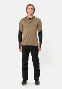Langarmtop met een half-rits, met een tan-kleurig lichaam en zwarte mouwen, gemaakt van gladde stof. Gecombineerd met zwarte slim-fit broeken en laarzen.