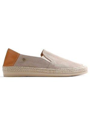 Chaussure beige en daim à enfiler avec une semelle intermédiaire en jute tressé, un talon en cuir marron clair, une semelle extérieure en caoutchouc plat, et un petit emblème métallique en forme de soleil sur le côté.