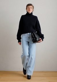Μαρίνα πλεχτή ζακέτα με ψηλό γιακά, ανοιχτό μπλε φαρδιά τζιν, μαύρη τσάντα χειρός και μαύρες μπότες. Απλές υφές και χαλαρή σιλουέτα.