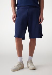 Marineblå atletiske shorts lavet af åndbart materiale, med et struktureret design, elastisk talje og sidelommer, parret med hvide sokker og sneakers.