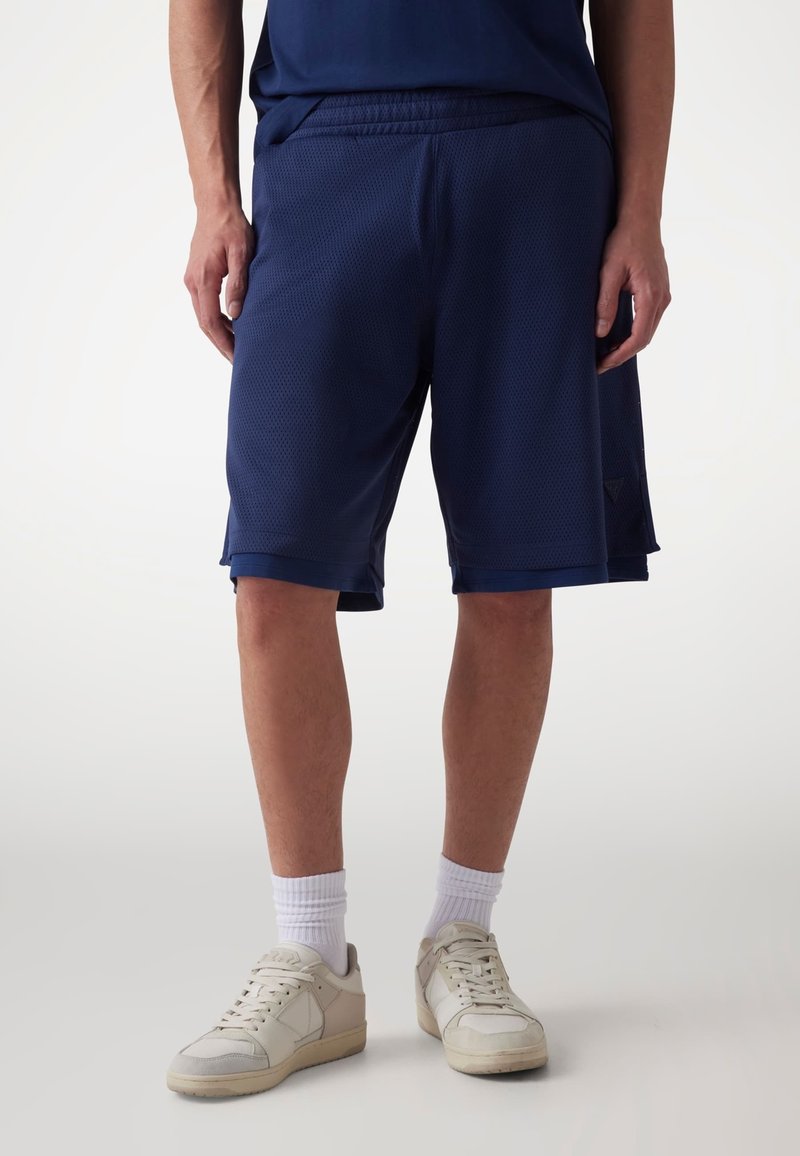 Shorts de sport bleu marine en tissu respirant, avec un design texturé, une taille élastique et des poches latérales, associés à des chaussettes blanches et des baskets.