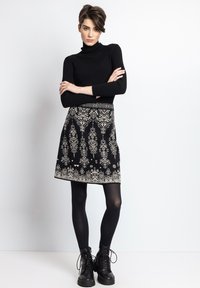 Crna rebrasta turtleneck majica uparenjena s crno-bijelim uzorkom suknje sa širim donjim dijelom. Model nosi crne tajice i robusne crne čizme s vezicama.