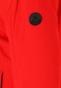 Tissu rouge vif avec un petit patch noir rond présentant des formes de montagnes et le mot Whistler au centre.