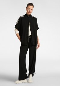 Haut noir surdimensionné avec zip, manches courtes et rayures blanches, associé à un pantalon noir avec rayures latérales et taille à cordon.