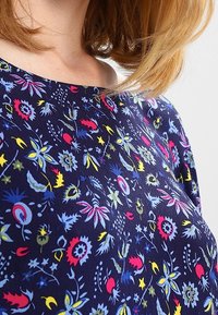Navy shirt featuring a floral pattern in red, blue, yellow, and white. The fabric has a smooth texture with a wide neckline and short sleeves.