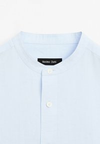 Camicia azzurro chiaro con colletto alla coreana. Presenta una superficie liscia e due bottoni frontali, con un'etichetta che recita "Massimo Dutti."