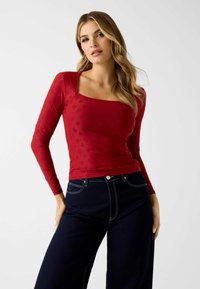 Rode top met lange mouwen en een vierkante halslijn, met een subtiel reliëfpatroon. Gecombineerd met high-waisted donker denim broek.