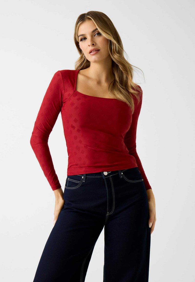 Rode top met lange mouwen en een vierkante halslijn, met een subtiel reliëfpatroon. Gecombineerd met high-waisted donker denim broek.