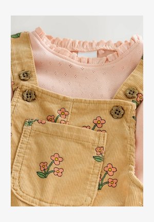 Barna kordbársony overall virágos hímzéssel a zsebnél, világos rózsaszín, hosszú ujjú felsővel, amely fodros nyakkivágással rendelkezik.