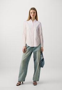Chemise légère rose pâle, coupe décontractée, avec des manches longues. Associée à un jean bleu clair à jambes larges et un petit sac en denim.