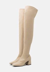 Botas beige hasta la rodilla hechas de material liso, con punta cuadrada y tacón grueso para mayor estabilidad. Detalles decorativos mínimos.