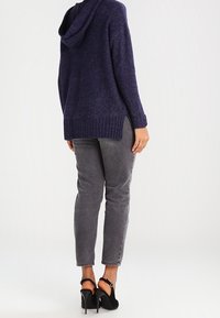 Sudadera con capucha de color navy con dobladillo acanalado y aberturas laterales, combinada con jeans ajustados grises y sandalias negras de tacón con tiras en el tobillo.