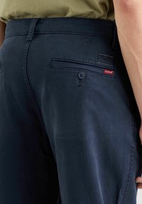 Granatowe spodnie z bawełny o gładkiej fakturze; wyposażone w guzik i tylnią kieszeń z etykietą Levi's.