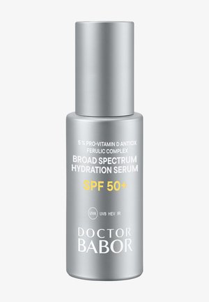 Sølvfarvet cylindrisk flaske med pumpe. Label indeholder produktnavn, SPF 50+ og vigtig information i sort og gul.