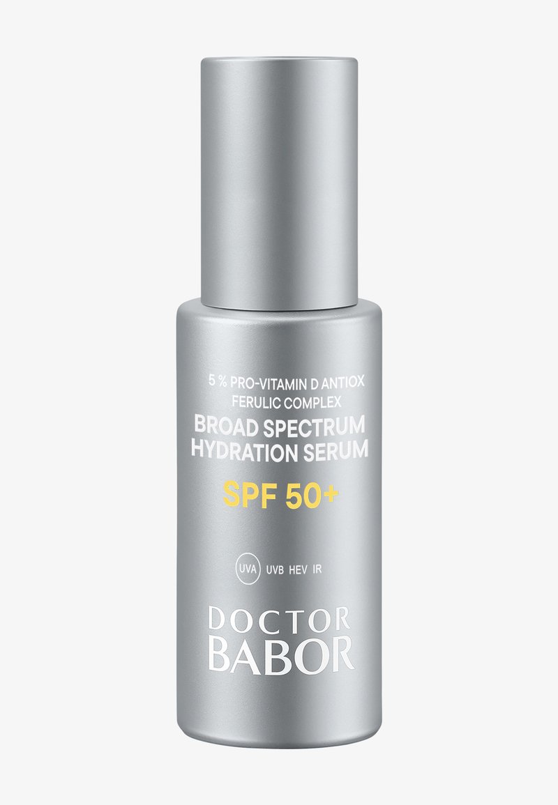 Flacon cylindrique argenté avec une pompe. L'étiquette comporte le nom du produit, SPF 50+, et des informations essentielles en noir et jaune.