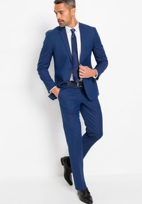 Completo blu con una vestibilità sartoriale, design a un petto, cravatta coordinata, camicia bianca e scarpe eleganti nere. Tessuto liscio e linee decise.