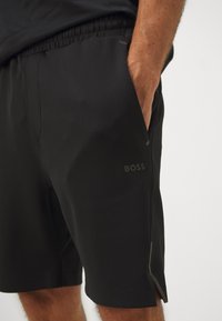 Pantalones cortos deportivos negros con una textura suave, que cuentan con una cinturilla elástica, bolsillos laterales y un pequeño detalle de logo en la parte frontal.