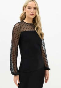 Zwarte top met lange doorzichtige mouwen met stippenpatroon. De lijfje is volledig zwart, met een gladde textuur en ronde halslijn.