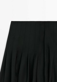 Jupe noire plissée avec des détails de coutures verticales et une taille haute sur fond blanc.
