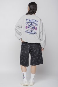 Sudadera gris con estampado gráfico en la parte posterior, combinada con pantalones cortos negros con un patrón. Calcetines blancos y zapatillas completan el conjunto.
