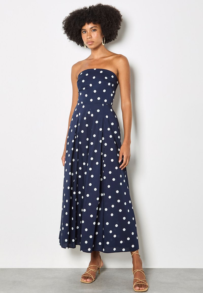 Robe longue bustier bleu marine à pois blancs, corsage ajusté, jupe évasée et tissu lisse. Design simple avec un motif classique.