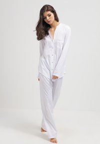 Vit pyjamas-set med långärmar i mjukt material. Har en knappstängning framtill och en bröstficka. Lös passform med raka byxor.