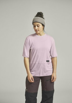 Light pink short-sleeve shirt with a relaxed fit, featuring a horizontal seam and small black label; worn with dark brown and black pants.