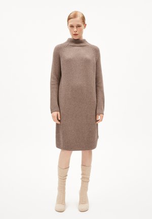 Knit dress in soft brown with a high neck and long sleeves, featuring a loose fit and ribbed texture. Worn with knee-high cream socks.