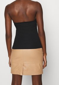 Svart, ribbad off-shoulder topp i kombination med en beige, läderminikjol med en slits bak. Slät textur genomgående.