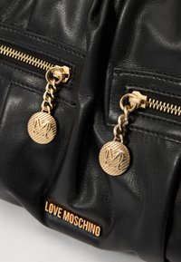 Černá kožená kabelka s zlatým kováním, dvěma zipovými táhly s kulatými přívěsky a embosovaným logem "LOVE MOSCHINO" na přední straně.