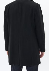 Musta villatakki suoralla leikkauksella, pitkät hihat ja ilman näkyvää metalliosaa; takana on keskiventtiili liikkumisen helpottamiseksi.