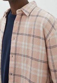 Chemise en flanelle à carreaux doux en rose pâle avec des checks blancs et marins, col boutonné, et boutons à l'avant, portée sur un t-shirt à col rond marine.