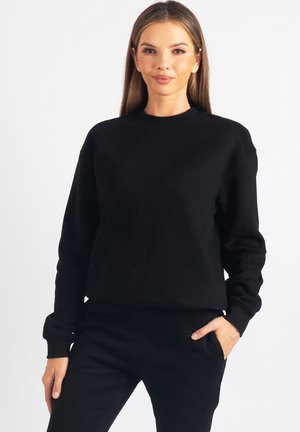 Czarna bluza z długimi rękawami, okrągłym dekoltem i luźnym krojem. Miękka tkanina i prążkowane ściągacze. W zestawie z dopasowanymi czarnymi spodniami.