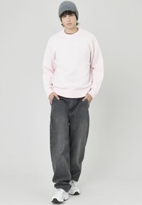 Pull tricoté rose clair avec poignets côtelés, associé à un jean ample gris foncé et des baskets blanches, complété par un bonnet en maille gris.