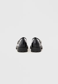 Black leather shoes with a rounded toe, chunky black rubber sole, and a decorative metallic buckle detail on the side.