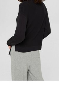 Maglione nero a maglia con un motivo testurizzato e polsini a costine, abbinato a pantaloni jersey grigio chiaro. Design aderente con fessure laterali.