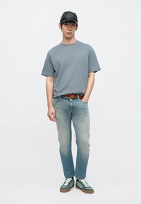 Γκρι βαμβακερό μπλουζάκι, ανοιχτό μπλε τζιν παντελόνι, καφέ δερμάτινη ζώνη και πράσινα αθλητικά παπούτσια με λευκά κορδόνια. Μαύρο καπέλο συμπληρώνει την εμφάνιση.