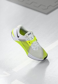 White and neon yellow athletic shoe with a mesh upper, black accents, and a textured sole. Features a lace-up design and prominent branding.