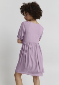Lila kurzärmeliges Kleid mit Rundhalsausschnitt, gerafftem Bund und fließendem Rock. Der Stoff wirkt strukturiert und leicht.