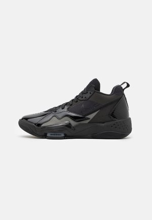 Baskets montantes noires de sport avec fermeture à lacets, semelle texturée et mélange de panneaux mats et brillants sur un fond clair uni.