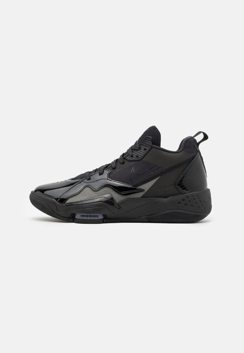 Baskets montantes noires de sport avec fermeture à lacets, semelle texturée et mélange de panneaux mats et brillants sur un fond clair uni.